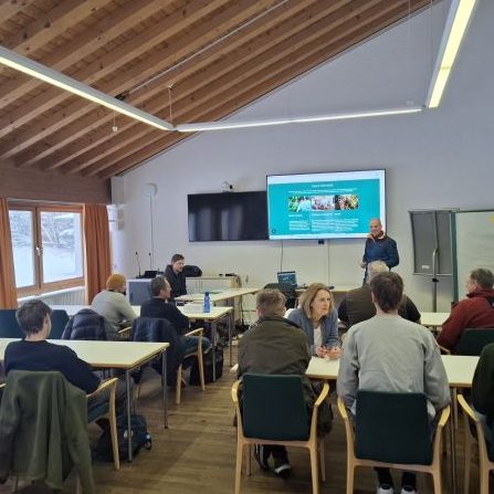 Zwei junge Frauen und ein Mann sitzen vor einem modernen Gebäude.