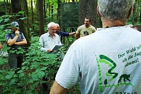  Eine Gruppe Menschen im Wald lauschen einem Förster.